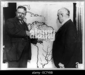 Le président Roosevelt en montrant une carte de l'Amérique du Sud vers la région d'examiner au cours de l'expédition scientifique au Brésil Roosevelt-Rondon comme un autre homme regarde. Theodore Roosevelt (1858 - 1919) était un homme politique américain, auteur, naturaliste, explorateur et historien qui a été le 26e président des États-Unis. Banque D'Images