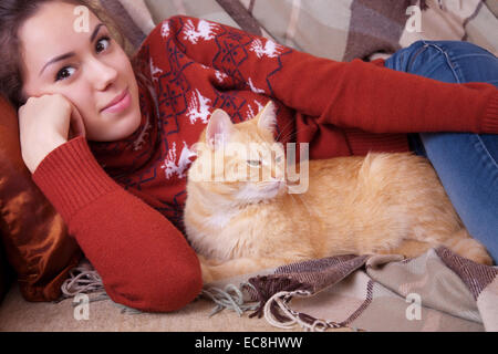 Jeune femme se reposer sur un canapé avec un chat rouge Banque D'Images