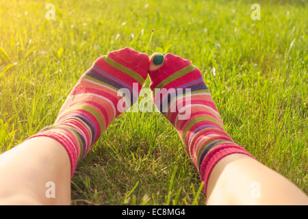 Teenage girl enjoying printemps allongé dans l'herbe, les pieds en chaussettes colorées déchirées, orteil peeping. Point de vue personnel, lens flare Banque D'Images