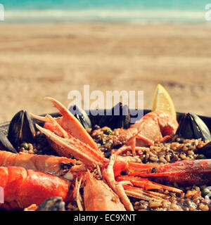 Une paella espagnole typique avec des fruits de mer dans une paellera, la paella pan, sur la plage, avec un effet rétro Banque D'Images