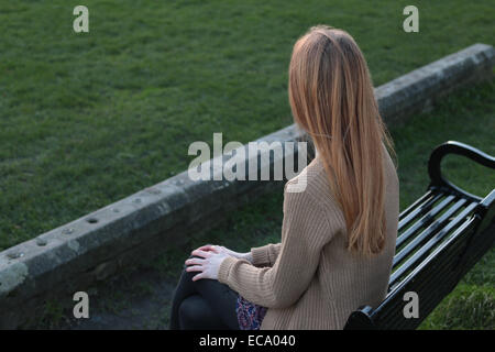 Vue arrière plan sur une jeune femme assise sur un banc, à la recherche dans la distance. Banque D'Images