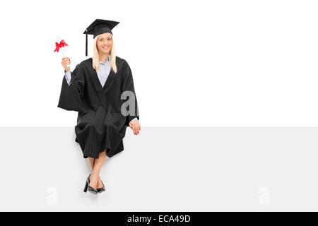 Happy female étudiant diplômé titulaire d'un diplôme assis sur un panneau vide isolé sur fond blanc Banque D'Images