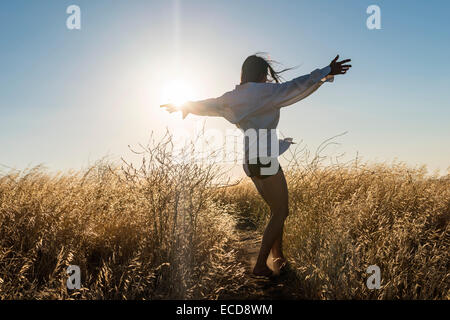 Femme dansant dans un champ d'herbe d'or dans les collines ensoleillées de Californie. Banque D'Images