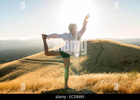 Woman in yoga pose dans un champ d'herbe d'or dans les collines ensoleillées de Californie. Banque D'Images