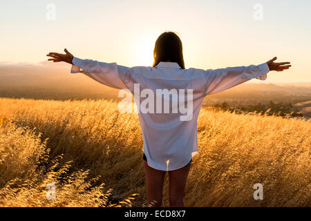 Femme debout dans un champ d'herbe d'or dans les collines ensoleillées de Californie. Banque D'Images