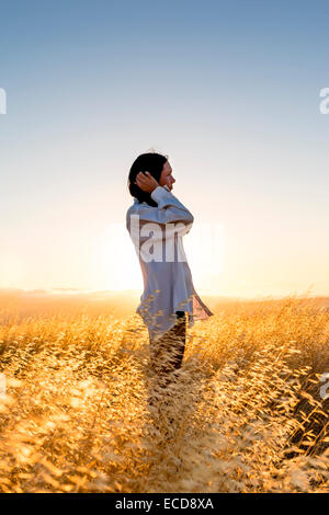 Femme debout dans un champ d'herbe d'or dans les collines ensoleillées de Californie. Banque D'Images