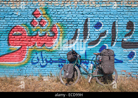 Vélos de cyclotourisme équipés de bouteilles d'eau dans les cages, les sacoches de guidon et quatre un sac en face de mur couvert de graffitis, l'Iran Banque D'Images