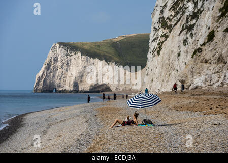 Une femme se trouve sous un parasol sur une plage sur la côte jurassique près de crique de Lulworth, dans le Dorset, en Angleterre, à côté de Durdle Door. Banque D'Images