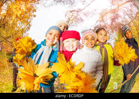 Les enfants positifs avec des tas de feuilles d'érable jaune Banque D'Images