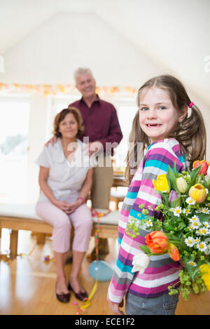 Petite-fille à sa grand-mère bouquet remise et grand-père en arrière-plan Banque D'Images