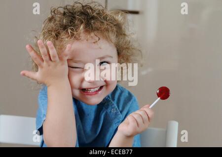 Bonne fille mangeant un lolipop et touchant son visage Banque D'Images