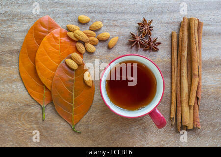 La vie encore des feuilles d'automne, graines d'amandes, tasse de thé, anis, girofle et cannelle sur la surface en bois Banque D'Images