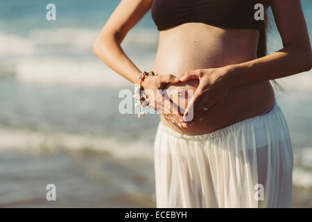 Pregnant Woman holding ses mains en forme de coeur sur son estomac Banque D'Images