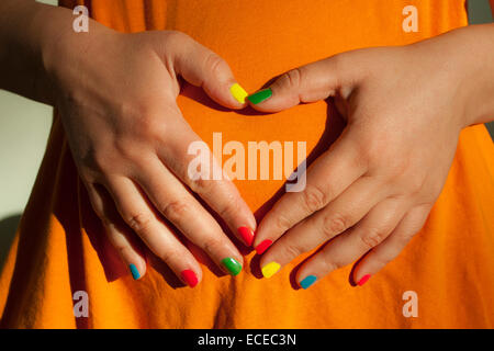 La mi-section shot of woman avec vernis à ongles multicolores en forme de coeur avec vos doigts contre ventre Banque D'Images