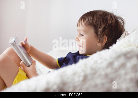 Un garçon souriant assis sur un canapé à l'aide d'une tablette numérique Banque D'Images