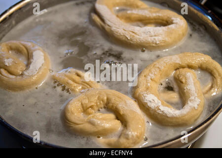 Close up of twisted soft pretzel dough le trempage dans un bain de sel chauffée dans une casserole sur la cuisinière avant cuisson Banque D'Images