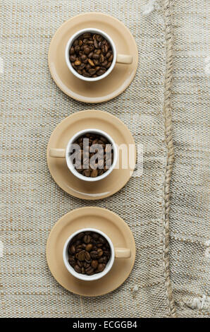 Les grains de café dans des gobelets sur toile rustique, vue ci-dessus Banque D'Images