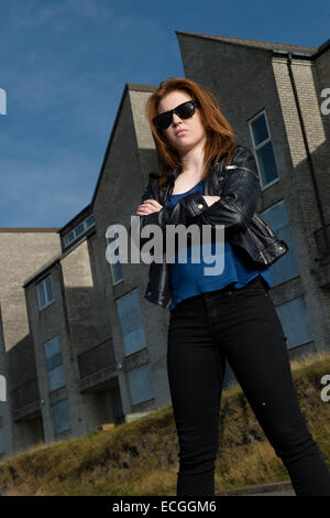 La culture des bandes : un solo Rousse aux cheveux moody gingembre jeune femme adolescent girl wearing sunglasses de défi permanent par elle-même en dehors d'un seul abandonné abandonné bloc d'appartements UK Banque D'Images