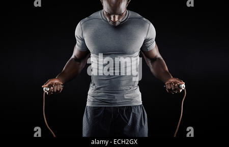 L'homme musclé la corde à sauter. Portrait of muscular young man exercising with jumping rope sur fond noir Banque D'Images