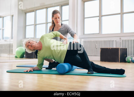 Instructeur féminin senior woman aidant à l'aide d'un rouleau en mousse pour un relâchement myofascial massage au sport. Banque D'Images