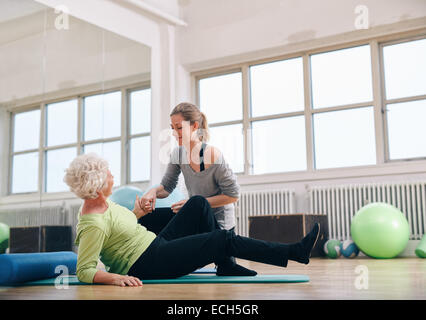 Female trainer helping old woman en passant d'un tapis d'exercice à la salle de sport. Senior woman étant assisté par instructeur personnel. Banque D'Images