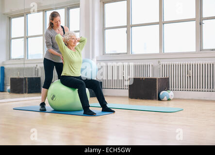 Hauts femme assise sur un ballon pilates de l'exercice au club de bien-être assistée par son entraîneur personnel. Thérapeute physique Banque D'Images