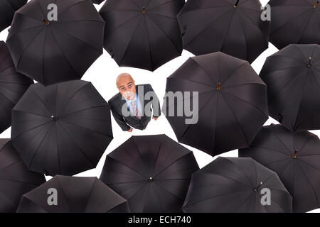 Businessman standing parmi les parapluies noir en blanc isolé Banque D'Images