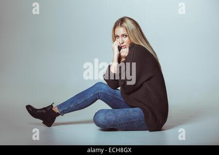 Portrait of attractive woman wearing sweater assis sur le plancher. Teenage girl looking at camera. Banque D'Images