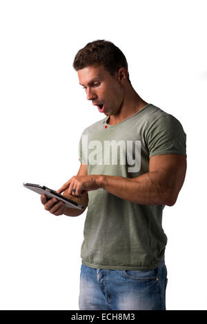 Muscular young man standing lors de la lecture d'e-livre avec expression surprise, isolated on white Banque D'Images