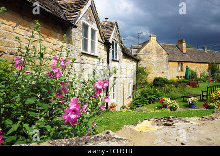 Cotswold stone cottages avec fleurs magenta dans le jardin. Banque D'Images