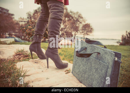 Photo vintage de femme jambes portant des bottes hautes et main sac près de l'herbe Banque D'Images