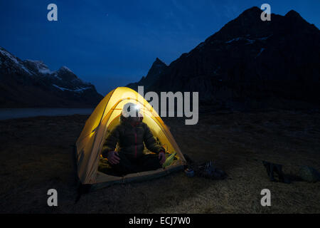 Female hiker est assis dans une tente éclairée la nuit, alors qu'au camping sauvage scenic Horseid plage, Moskenesøy, îles Lofoten, Norvège Banque D'Images