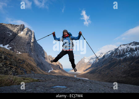 Female hiker saute dans l'air avec Horseid plage en arrière-plan, Moskenesøy, îles Lofoten, Norvège Banque D'Images