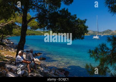 La Croatie, Dalmatie, parc national de Kornati, Dugi Otok, couple de retraités assis sur la rive, à l'ombre de pins qui envisagent un ruisseau où l'yachts amarrés Banque D'Images