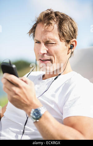 Homme mature portant des écouteurs lors de l'utilisation de smart phone outdoors Banque D'Images