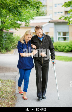 Toute la longueur de l'heureux gardien femelle marcher avec mobilité senior man on street Banque D'Images