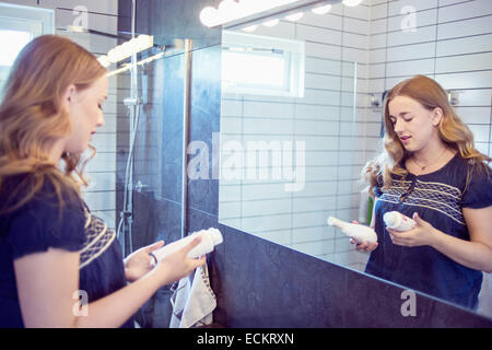 Jeune femme tenant des flacons de parfum en face du miroir de salle de bains Banque D'Images