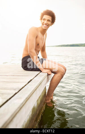 Happy young man looking away while sitting on demande par contre le lac Clear Sky Banque D'Images