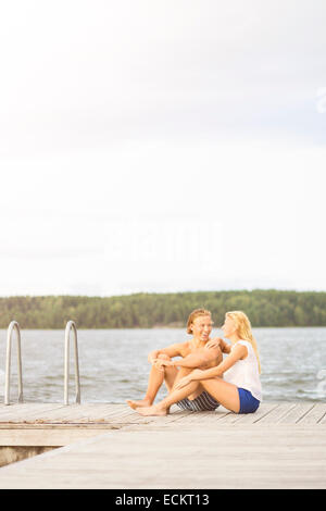 Couple sitting on boardwalk par lake against sky Banque D'Images