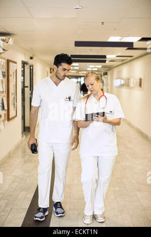 Longueur totale de médecins discutant sur digital tablet in hospital corridor Banque D'Images