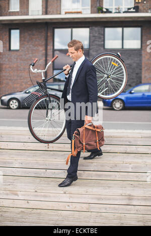 Toute la longueur du businessman carrying bicycle en marchant sur les mesures Banque D'Images