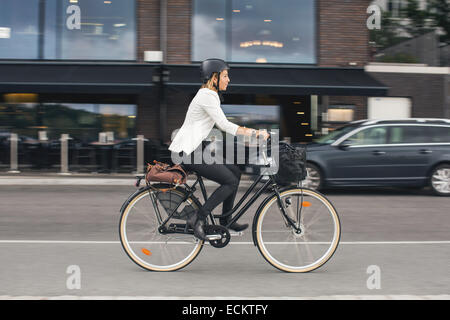 Toute la longueur de businesswoman riding bicycle on city street Banque D'Images