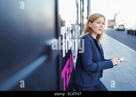 Businesswoman looking, tandis que l'aide de mobile phone on sidewalk Banque D'Images