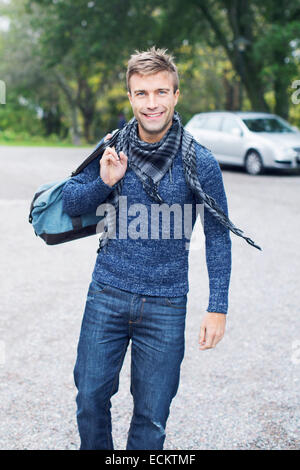 Portrait of smiling young man carrying bag on street Banque D'Images