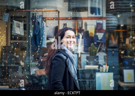 Side view portrait of smiling woman standing against shop Banque D'Images