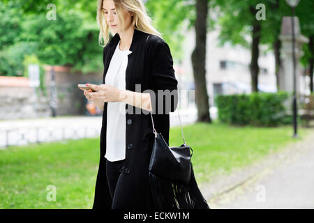 Jeune femme à l'aide de téléphone portable en marche sur sentier au parc Banque D'Images