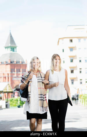 Smiling female friends walking avec bras dessus bras dessous on city street Banque D'Images