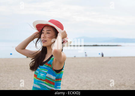 Une femme sur une plage à Kobe tenant son chapeau sur la tête. Banque D'Images