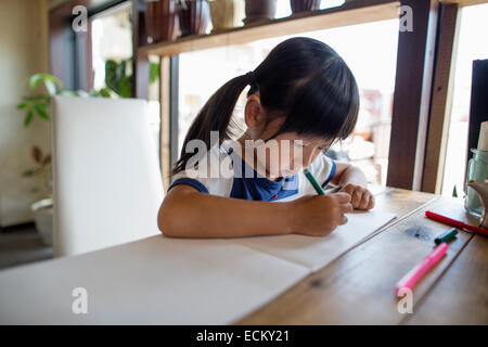 Fille avec des tresses assis à une table, dessin avec feutres. Banque D'Images