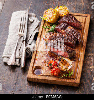 Tranches de steak de boeuf grillée saignante Ribeye avec le maïs et tomates cerises sur une planche à découper sur fond de bois Banque D'Images